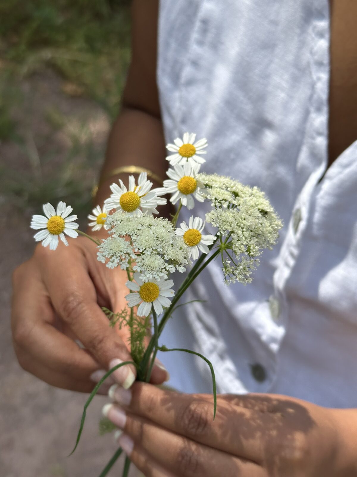 A small bouquet of flowers held by the fingertips of a woman in a white shirt.